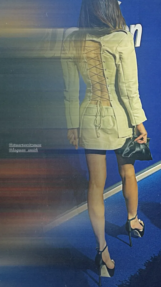 Sarah Shahi posing at a sporting event in a pale jacket dress.