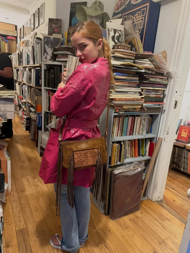Addison Rae a mirror portrait in jeans and a pink top beside shelves of records.