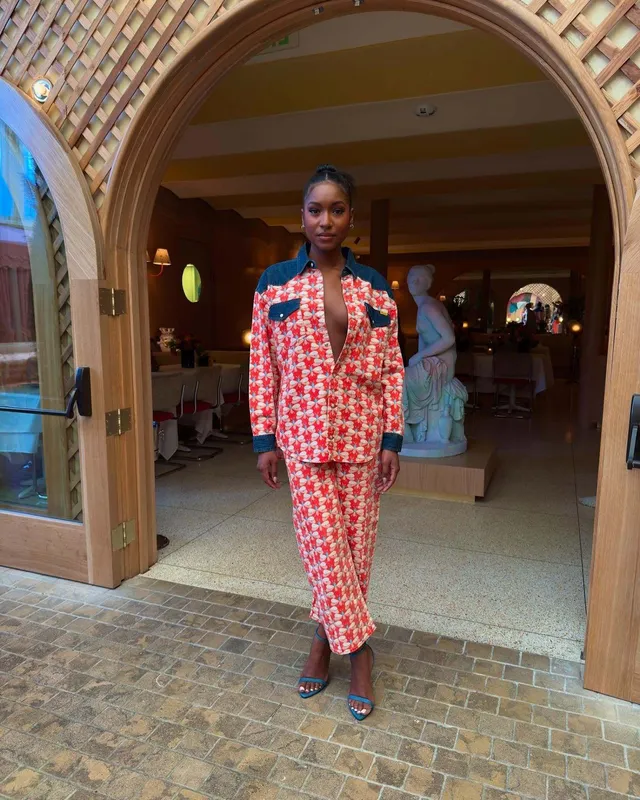 Carlacia Grant walking through an archway in a patterned suit and heels.