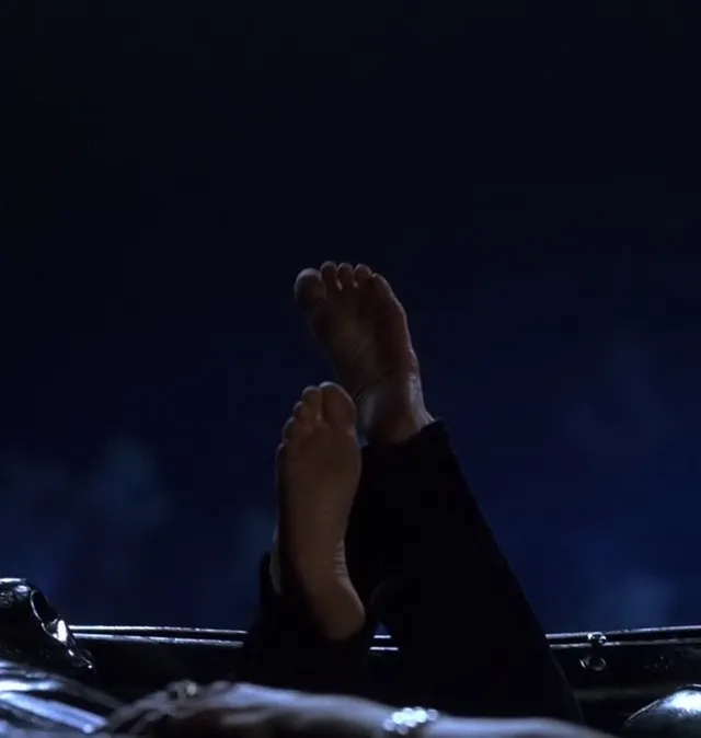 Anne Hathaway raising bare soles in a dark screen scene.