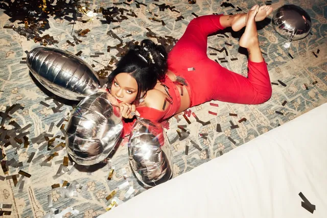Rihanna posing on a patterned floor in a red top and black high-heeled boots.