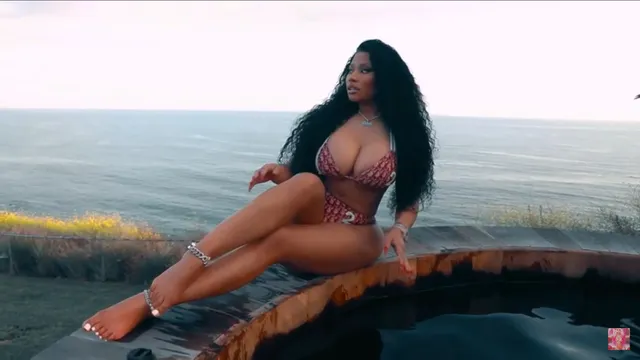 Nicki Minaj sitting barefoot beside a swimming pool.