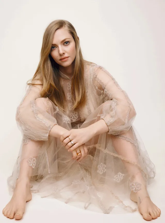 Amanda Seyfried sitting barefoot in a pale flowing outfit.