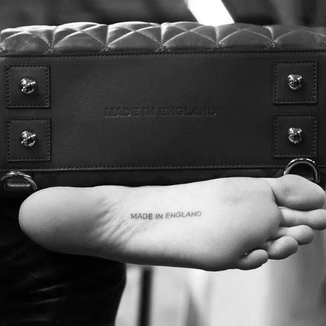 Cara Delevingne showing a foot tattoo in a monochrome studio photograph.
