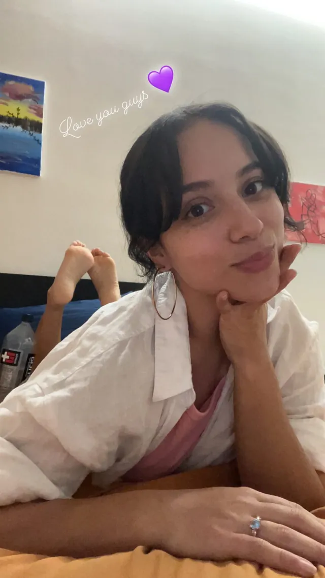Kiana Madeira reclining barefoot indoors in a white shirt and pink top.