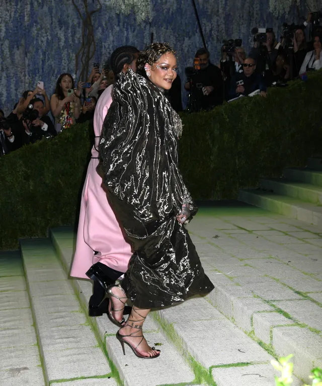 Rihanna walking up steps in an embellished coat and strappy heels.