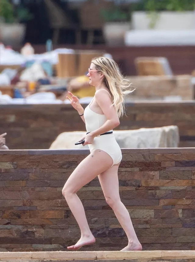Emma Roberts walking barefoot beside an outdoor stone wall.