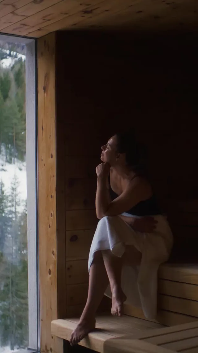 Maria Sharapova sitting barefoot beside a window in a dim room.
