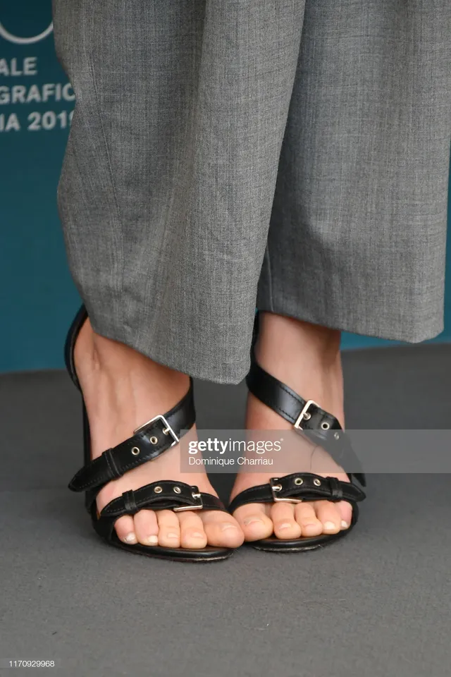 Scarlett Johansson wearing black sandals beneath gray trousers.
