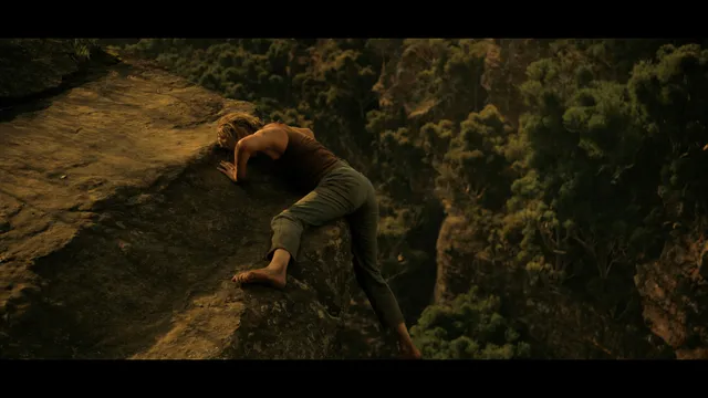 Charlize Theron a screen scene climbing across a rocky ledge.