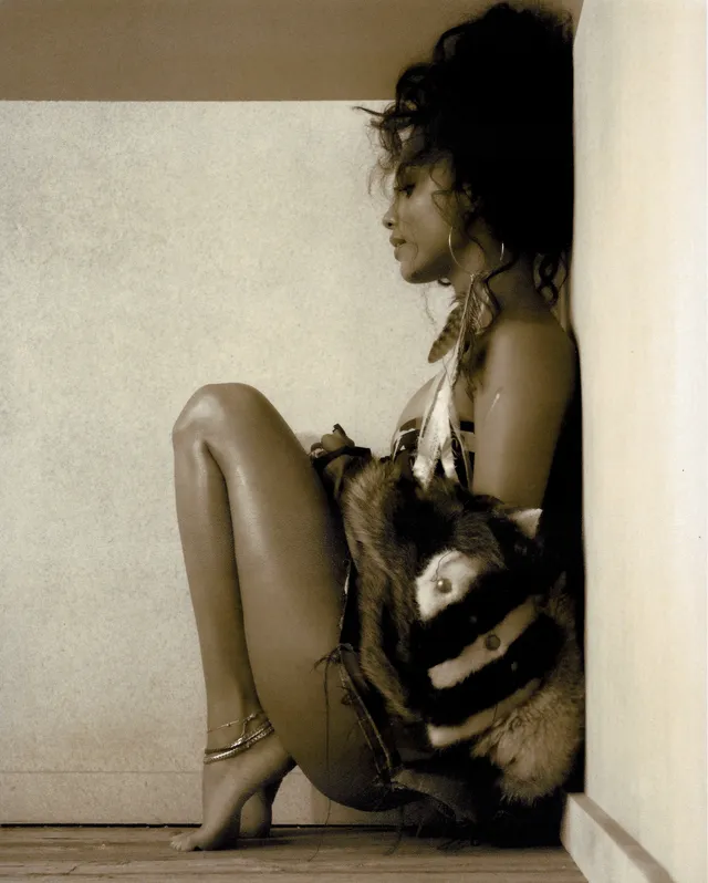 Tyla crouching in heels and a patterned outfit during a warm-toned studio portrait.