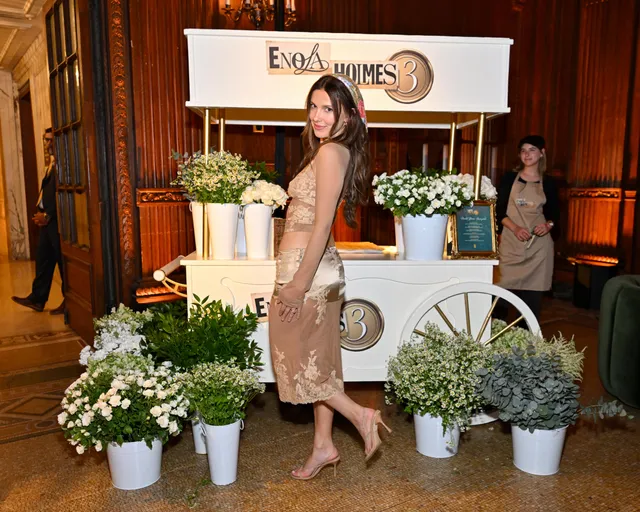 Millie Bobby Brown posing beside an event display in a pale dress.