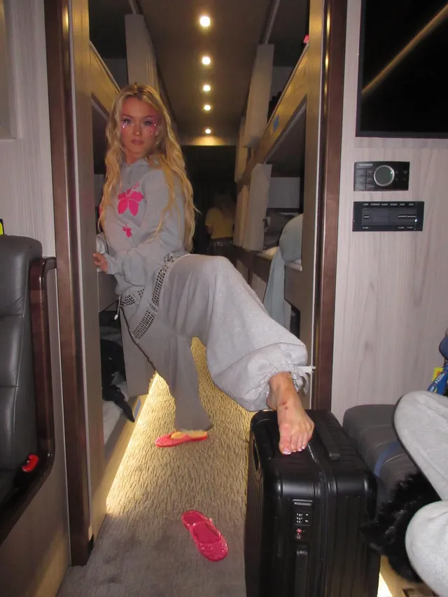 Zara Larsson resting a bare foot on luggage in a train corridor.