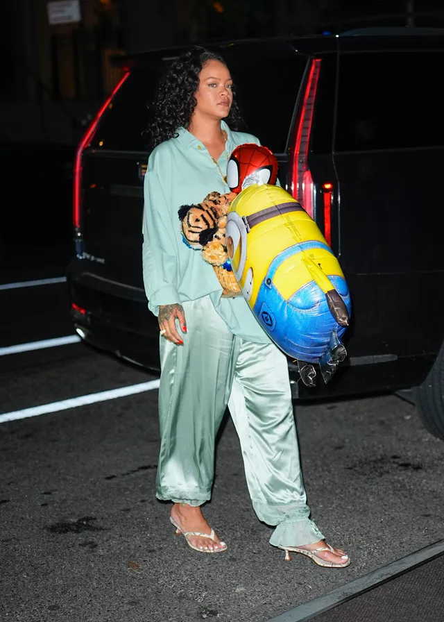 Rihanna standing beside a vehicle in a green outfit and clear heels.
