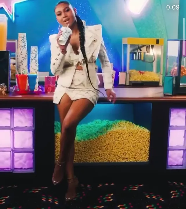 Sierra Capri posing on a studio counter in a white outfit and heels.