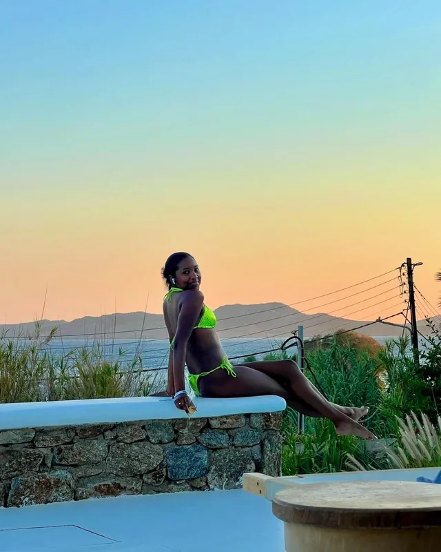 Carlacia Grant sitting barefoot on an outdoor bench in a green bikini.