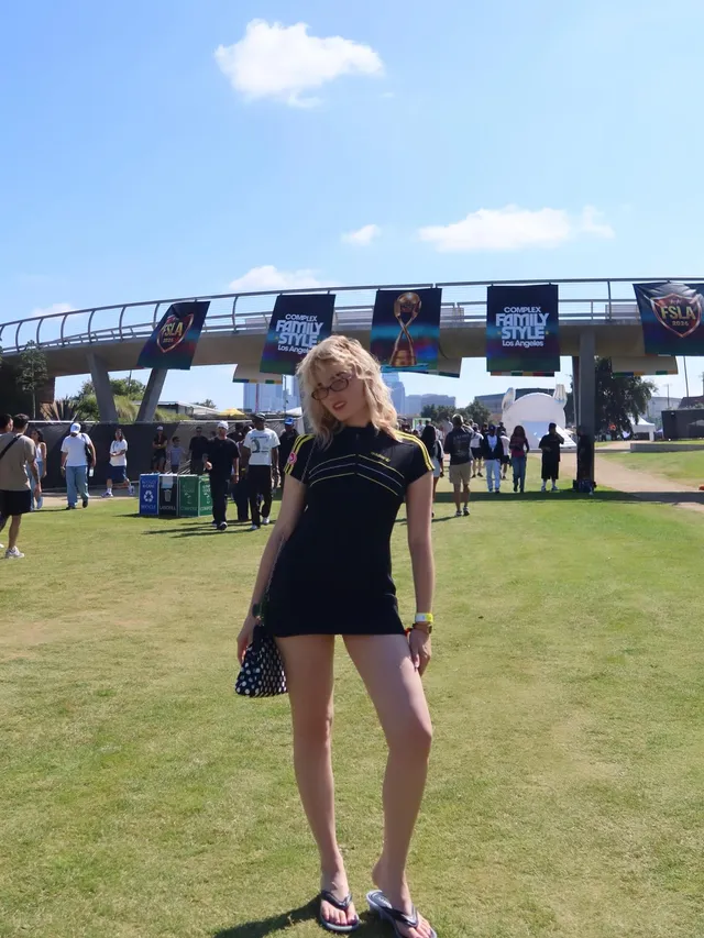 Meg Donnelly standing on grass in a black outfit and dark sneakers.