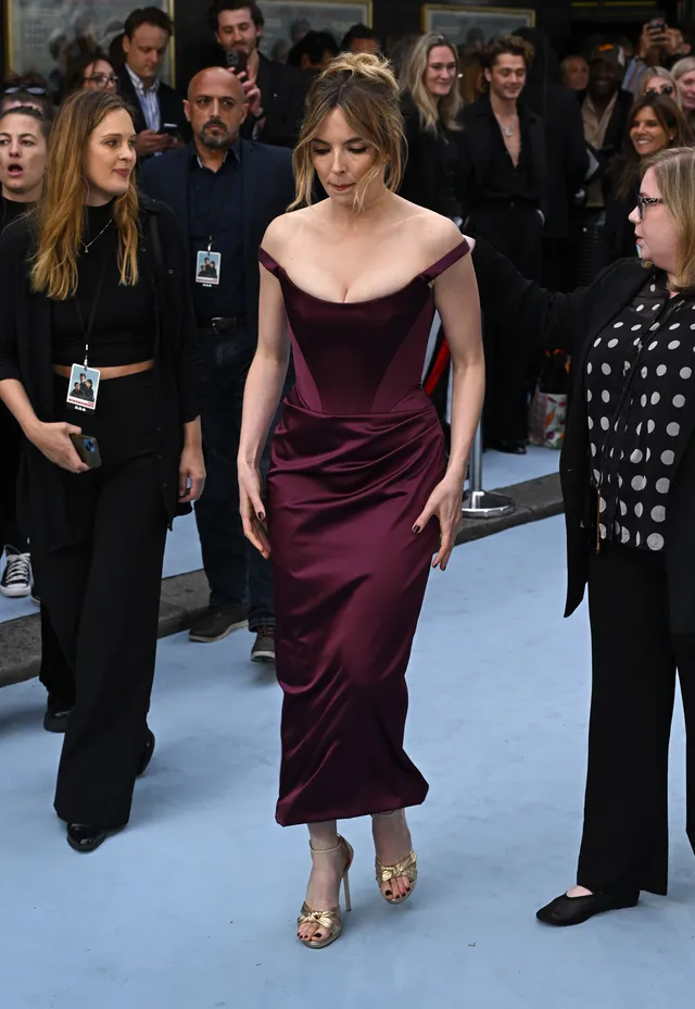 Jodie Comer walking on a carpet in a burgundy evening dress.