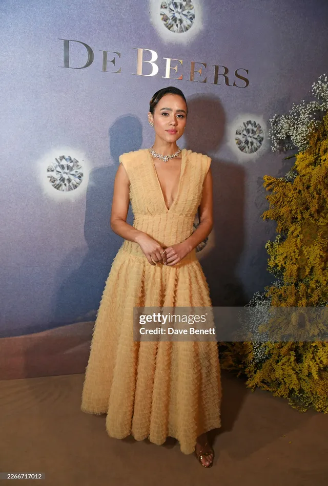Nathalie Emmanuel posing against a jewellery event backdrop.