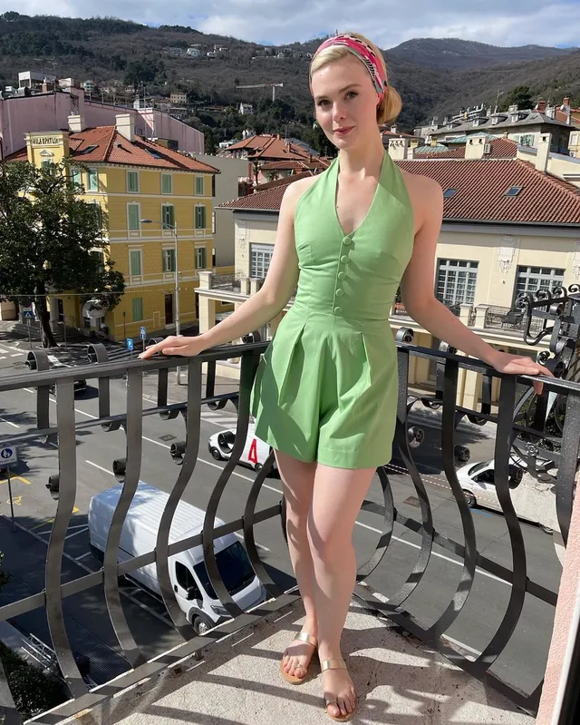 Elle Fanning posing barefoot on a balcony in a green outfit.