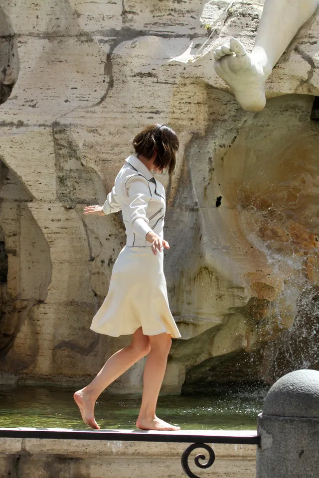 Úrsula Corberó walking barefoot outdoors in a pale dress.