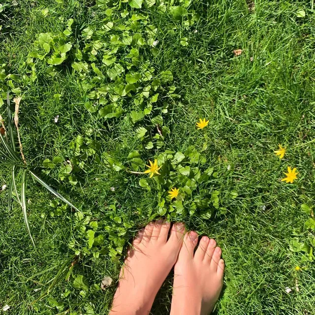 Miranda Kerr bare feet among yellow flowers on grass.
