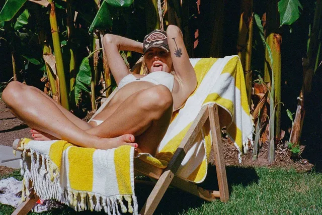 Samara Weaving relaxing barefoot on a striped garden lounger.