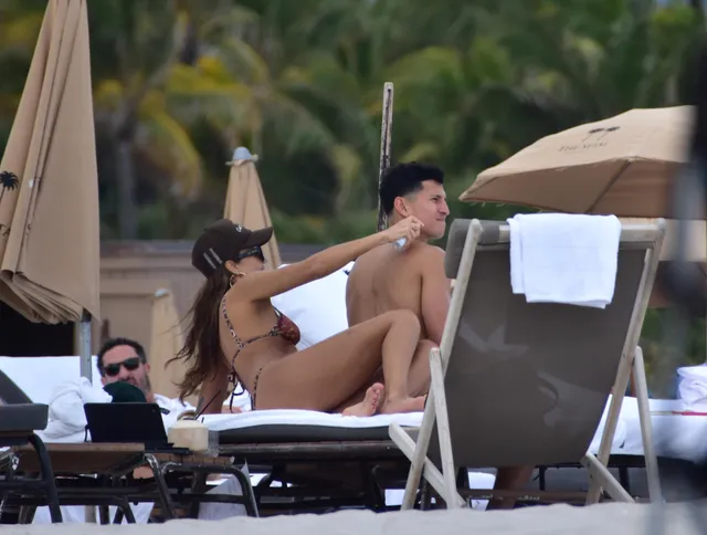 Jessica Alba sitting barefoot on a sun lounger beside another person.