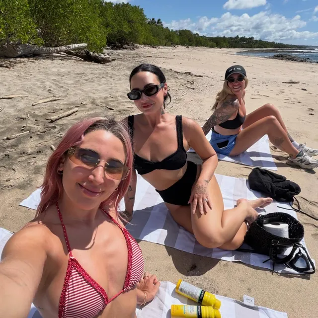 Demi Lovato sitting barefoot on a beach with other people.