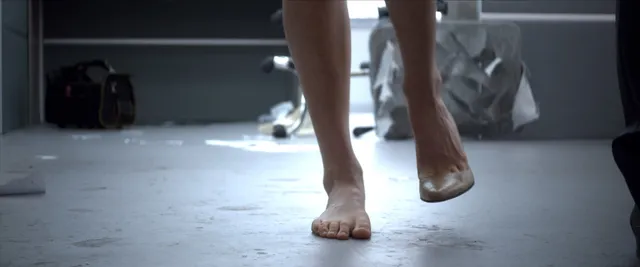 Samara Weaving stepping barefoot across an indoor floor in a film scene.