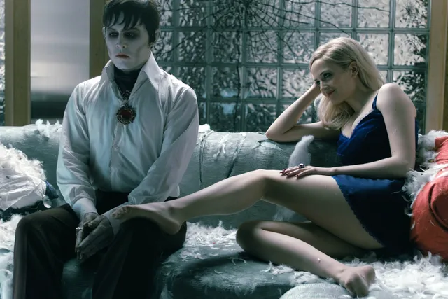 Eva Green a seated screen scene on a sofa beside another character.