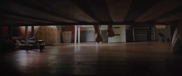 Chloë Grace Moretz showing bare feet beneath a bed in a film scene.
