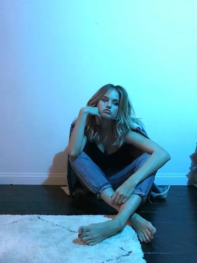 Debby Ryan sitting barefoot indoors in blue light.