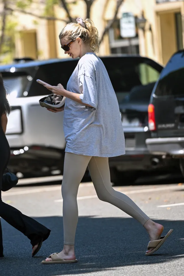 Elsa Hosk walking outdoors in pale flat sandals with a blue shirt.