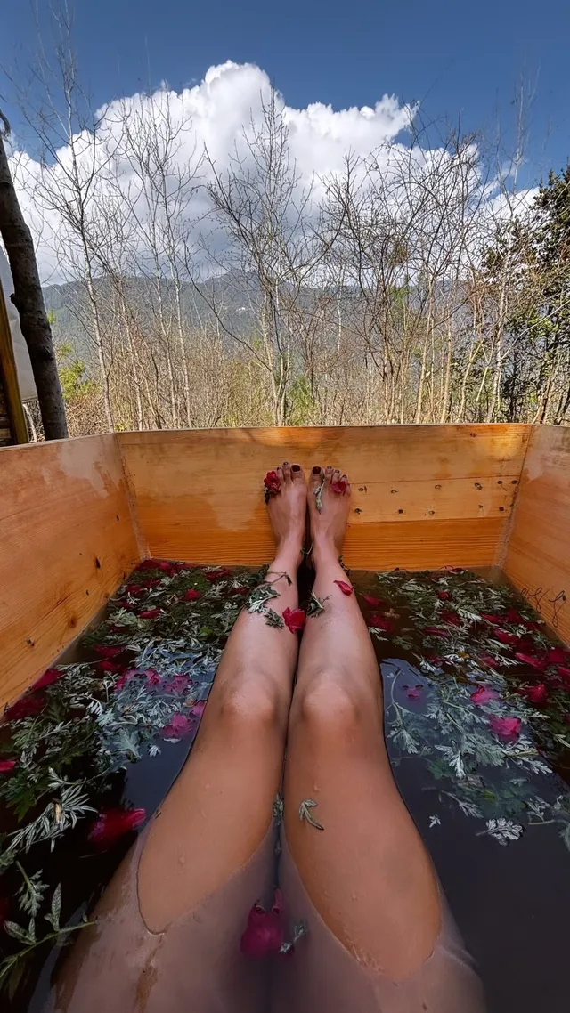 Tessa Thompson relaxing in an outdoor bath with flower petals.