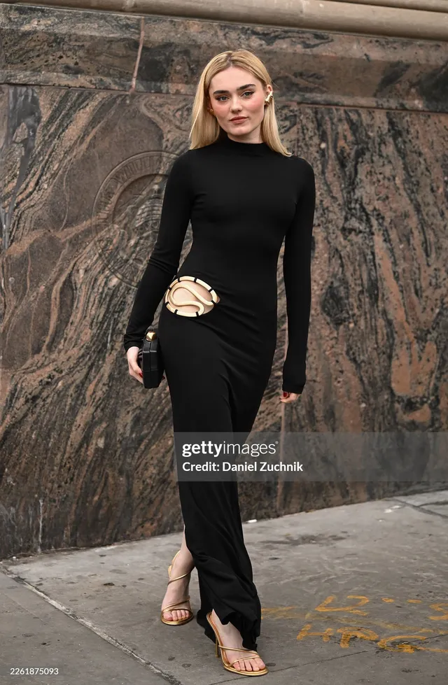 Meg Donnelly wearing a long black outfit and flat sandals outside a building.