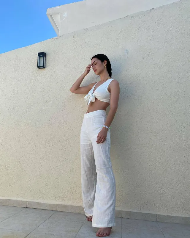 Adelaide Kane posing beside a wall in a white outfit.