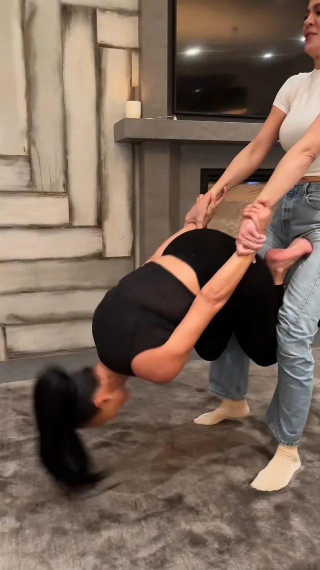 Kim Kardashian lying on a carpet while a companion holds her hands.