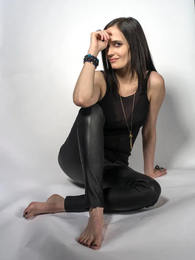 Eva Green seated against a pale backdrop in a black outfit.