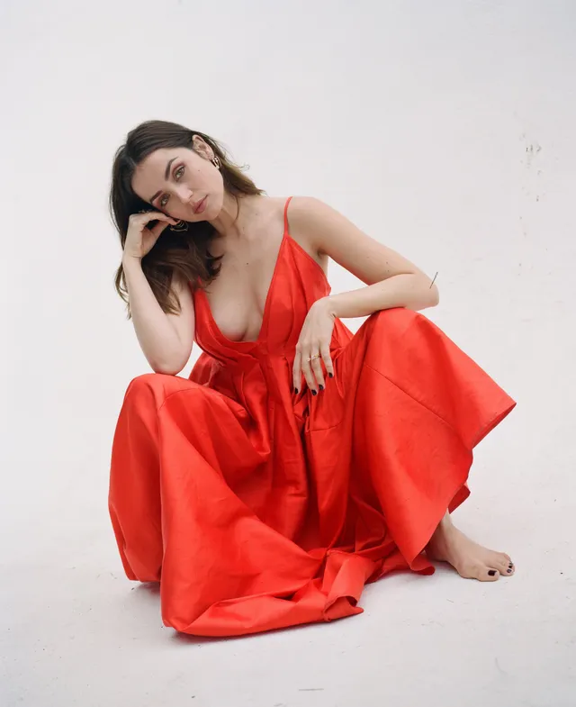 Ana de Armas: seated barefoot in a flowing red dress.