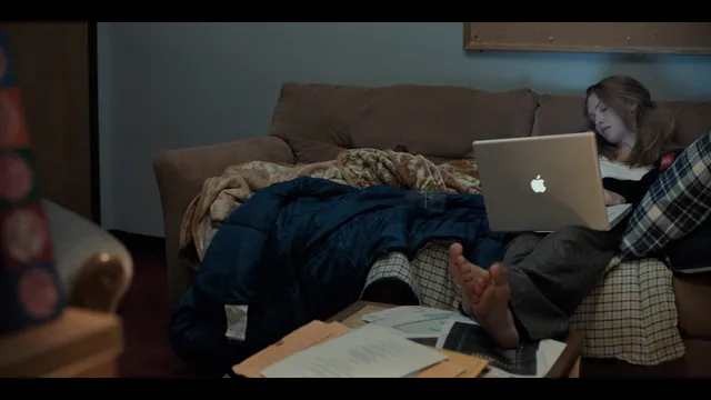 Amanda Seyfried reclining barefoot on a couch with a laptop in a screen image.
