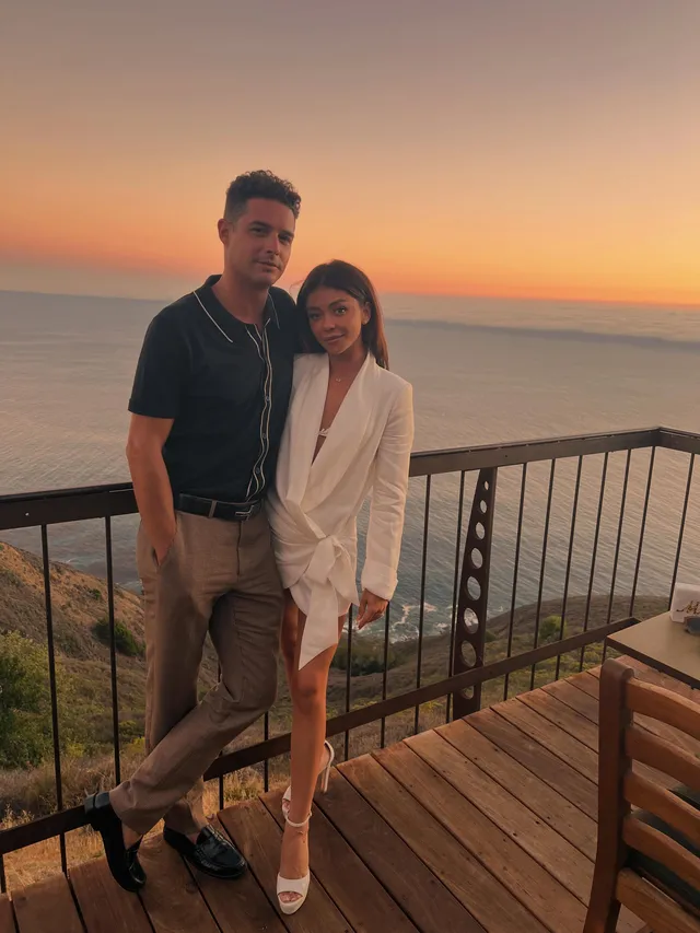Sarah Hyland standing beside a companion on a balcony at sunset.