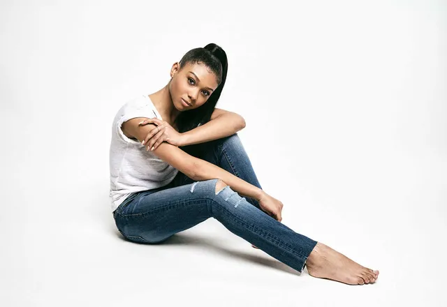 Sierra Capri sitting barefoot in jeans and a white top for a studio portrait.