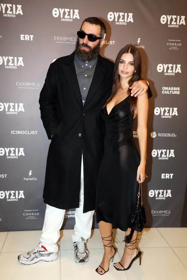 Emily Ratajkowski posing beside a man wearing a long black dress and heels.
