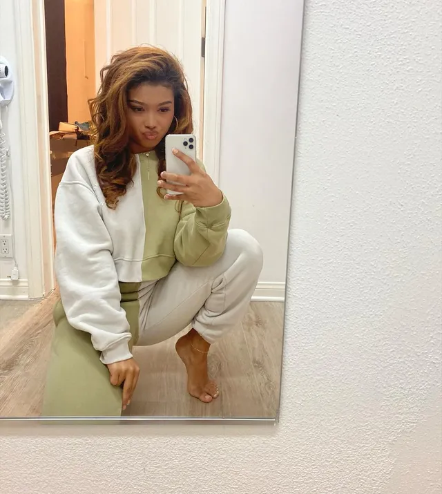 Sierra Capri crouching barefoot in a pale tracksuit in front of a mirror.