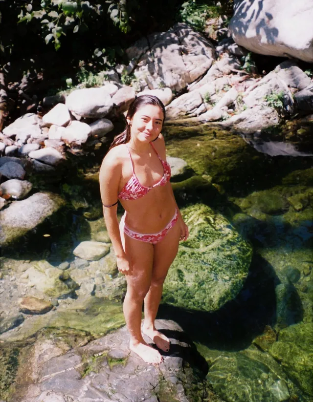 Xochitl Gomez standing barefoot beside a rocky stream.