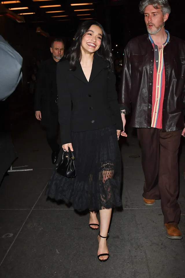 Rachel Zegler walking beside a man in a black lace dress and heels.