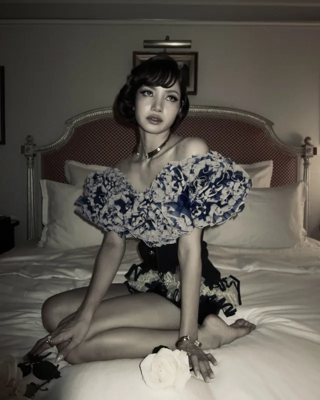Lisa (Lalisa Manobal) kneeling barefoot on a bed in a floral-collar outfit during a monochrome portrait.