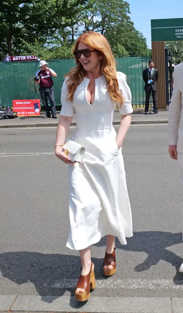 Isla Fisher walking outdoors in a white outfit and wedge sandals.
