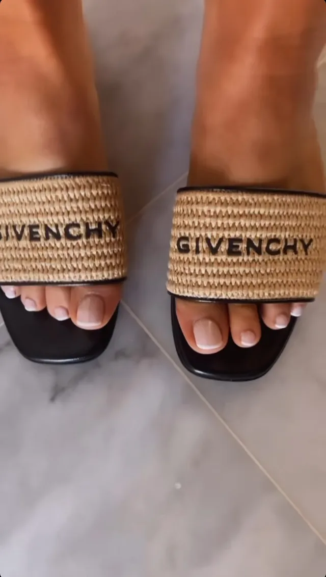 Bebe Rexha showing dark sandals with woven branded straps.